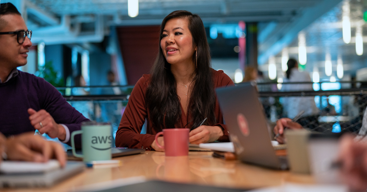 People engaged in a team collaboration meeting at an AWS office, with laptops and coffee mugs on the table.