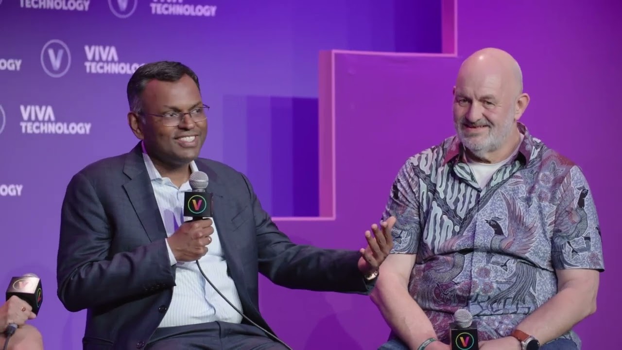 Two speakers participate in a panel discussion at Viva Technology, seated on stage with microphones and a purple backdrop featuring event branding.