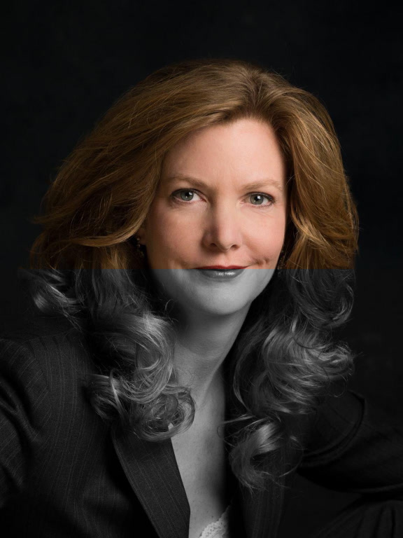A person with long, wavy auburn hair wearing a dark pinstripe blazer against a black background.