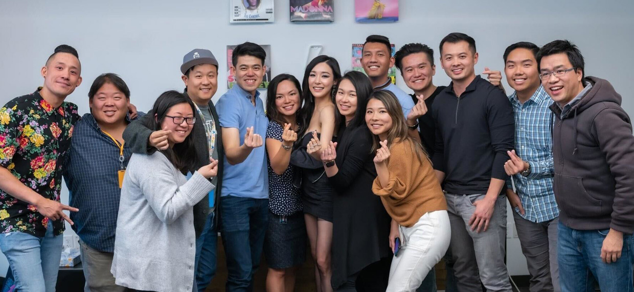 A group of AWS employees from the Asian American and Pacific Islander (AAPI) employee resource group celebrating together. The group stands in a row smiling and making heart gestures with their hands.