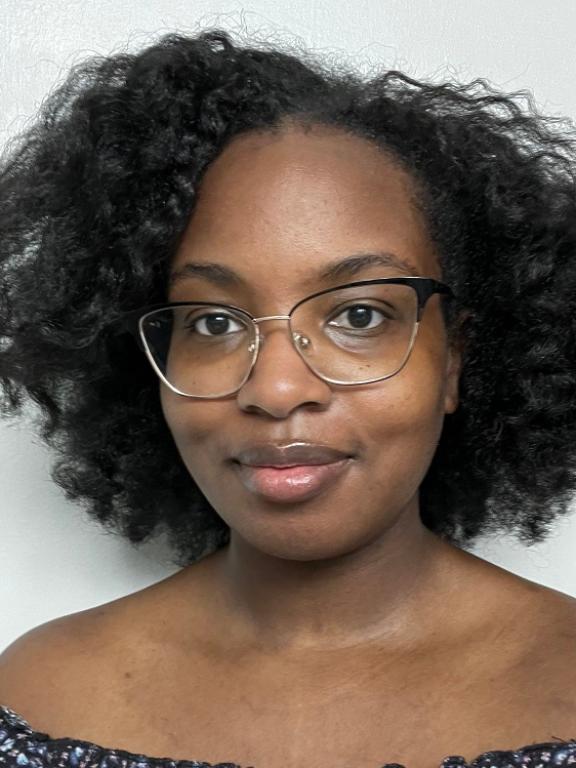 A professional portrait of a person with natural curly hair wearing glasses, set against a plain background.