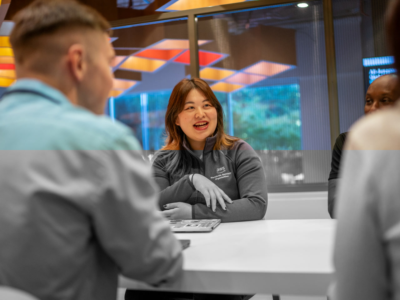 An AWS employee collaborates with colleagues around a table in a modern Amazon office setting.