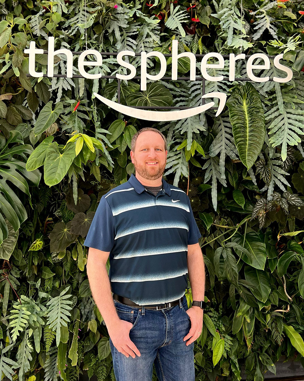 A person standing in front of a vertical green wall of plants at Amazon's The Spheres, with a sign reading 'the spheres' above.