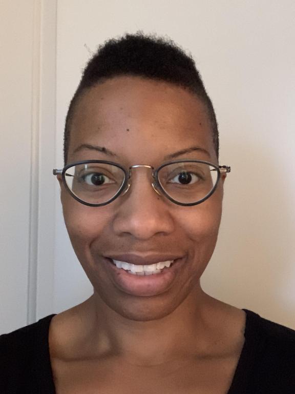 A portrait of a person wearing glasses and smiling in front of a neutral background.