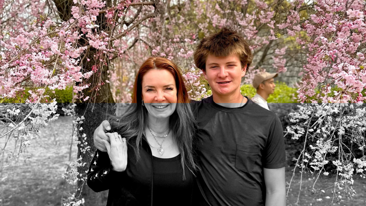 A woman and a boy are standing together, smiling, beneath a blooming pink tree outdoors. The background features vibrant pink blossoms and a soft, natural setting.