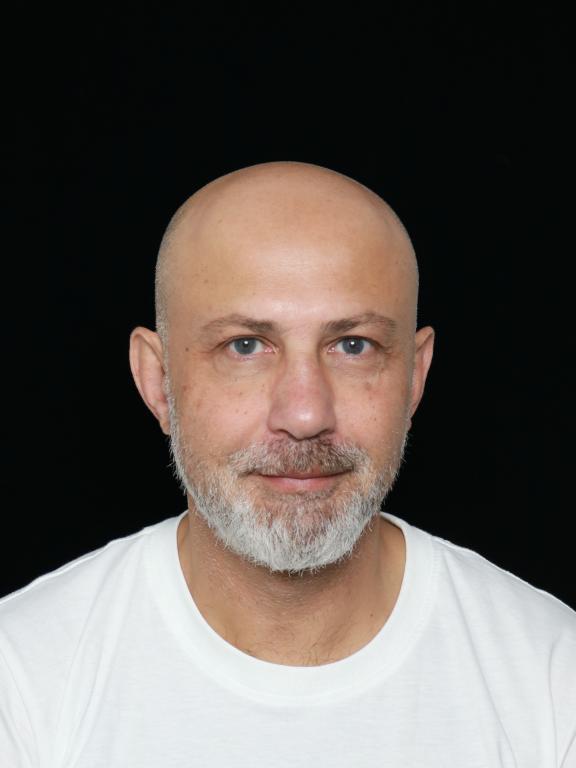 Portrait of a bald man with a beard wearing a white shirt against a black background.