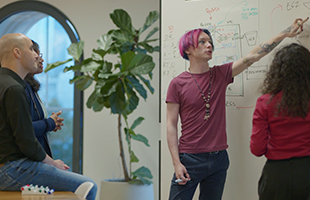 A group of AWS developers collaborating and discussing ideas in front of a whiteboard in an office setting.