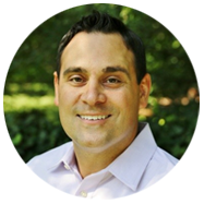 2A person wearing a light purple collared shirt, standing outdoors with greenery in the background.2