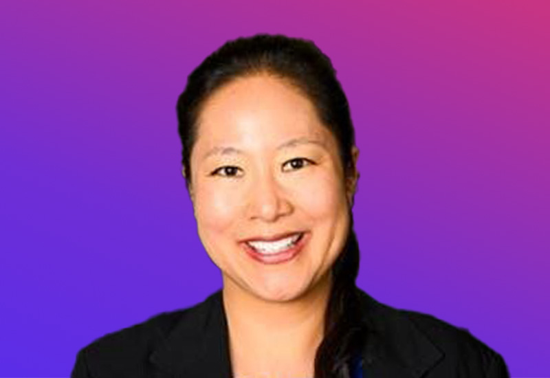 A person wearing a black blazer against a gradient purple and pink background.