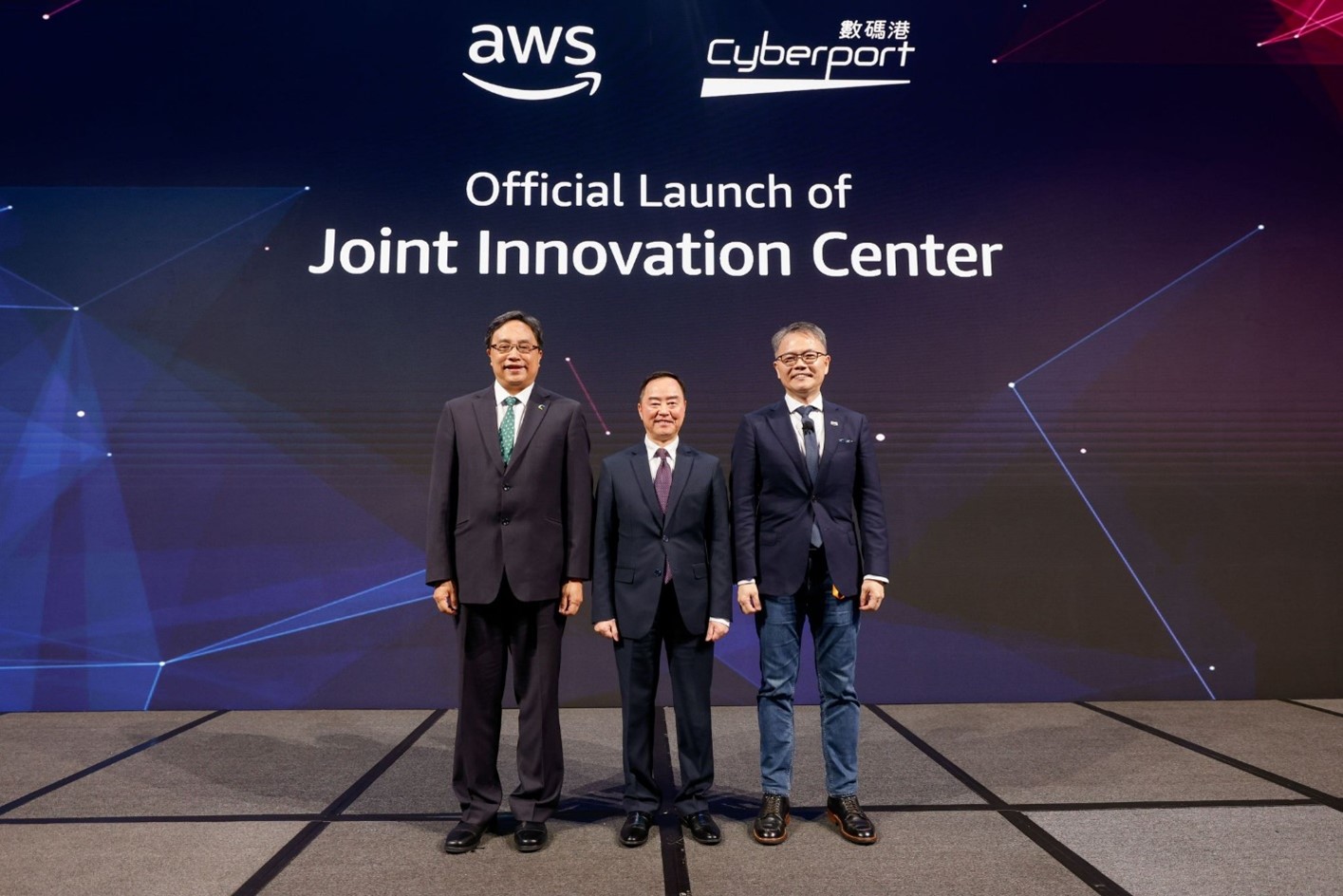 Three individuals stand on stage in front of a screen displaying the text 'AWS', 'Cyberport', and 'Official Launch of Joint Innovation Center' during the launch event.