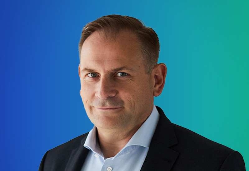 A person in formal attire with a gradient blue and green background.