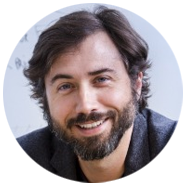 2A person with shoulder-length dark hair wearing a gray blazer.