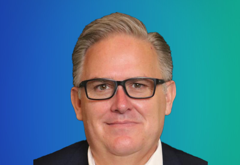 A professional headshot of a person with glasses and short gray hair, in business attire, set against a blue-green gradient background.