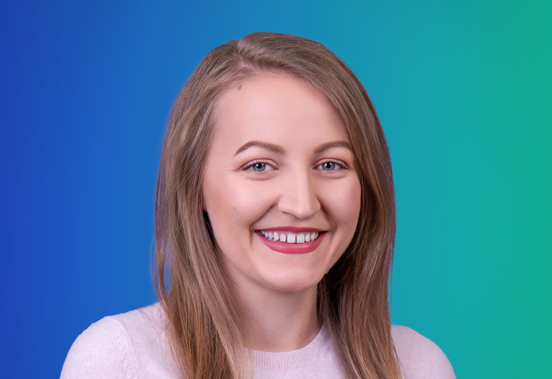 A professional headshot of a smiling woman with long light brown hair, wearing a light sweater, in front of a blue and green gradient background.