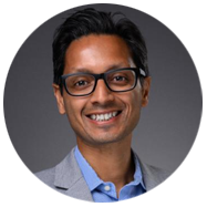 2A person wearing a light gray blazer and blue collared shirt against a dark gray background.