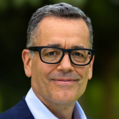 Professional portrait of a man in glasses and a suit, with a blurred green background.