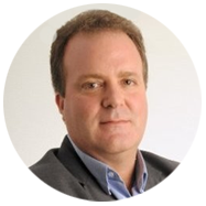 2A person wearing a suit jacket and collared shirt against a plain background.