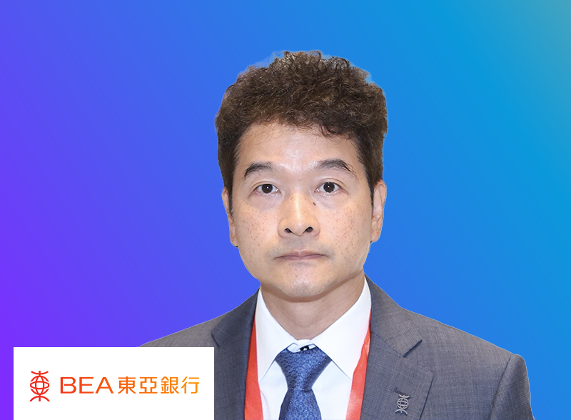 A professional portrait of a man in a business suit with a red lanyard, set against a blue gradient background. The BEA East Asia Bank logo and name are visible in the bottom left corner.