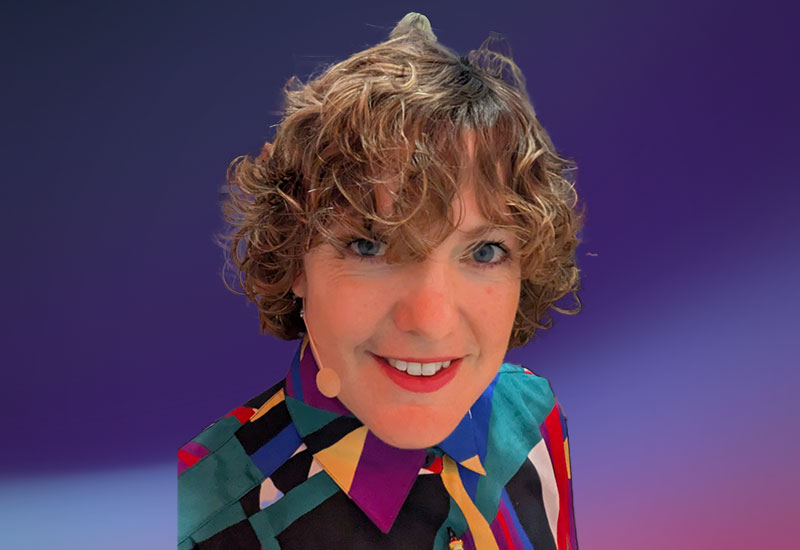 A person with curly hair wearing a colorful, geometric-patterned shirt against a gradient purple background.