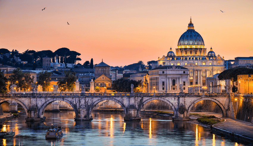A scenic view of St. Peter's Basilica and the Tiber River in Rome at sunset, with the city lights reflecting on the water and birds in the sky.