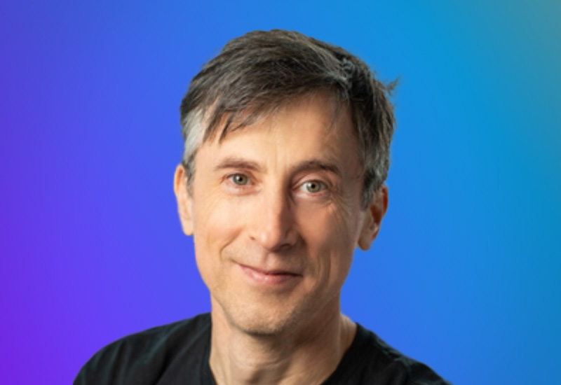 A person with short gray hair against a gradient blue and purple background.