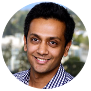 2A person wearing a checkered shirt with a blurred background of trees and buildings.