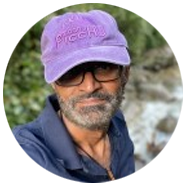 2A person wearing a purple cap and a dark shirt, with a blurred natural background.