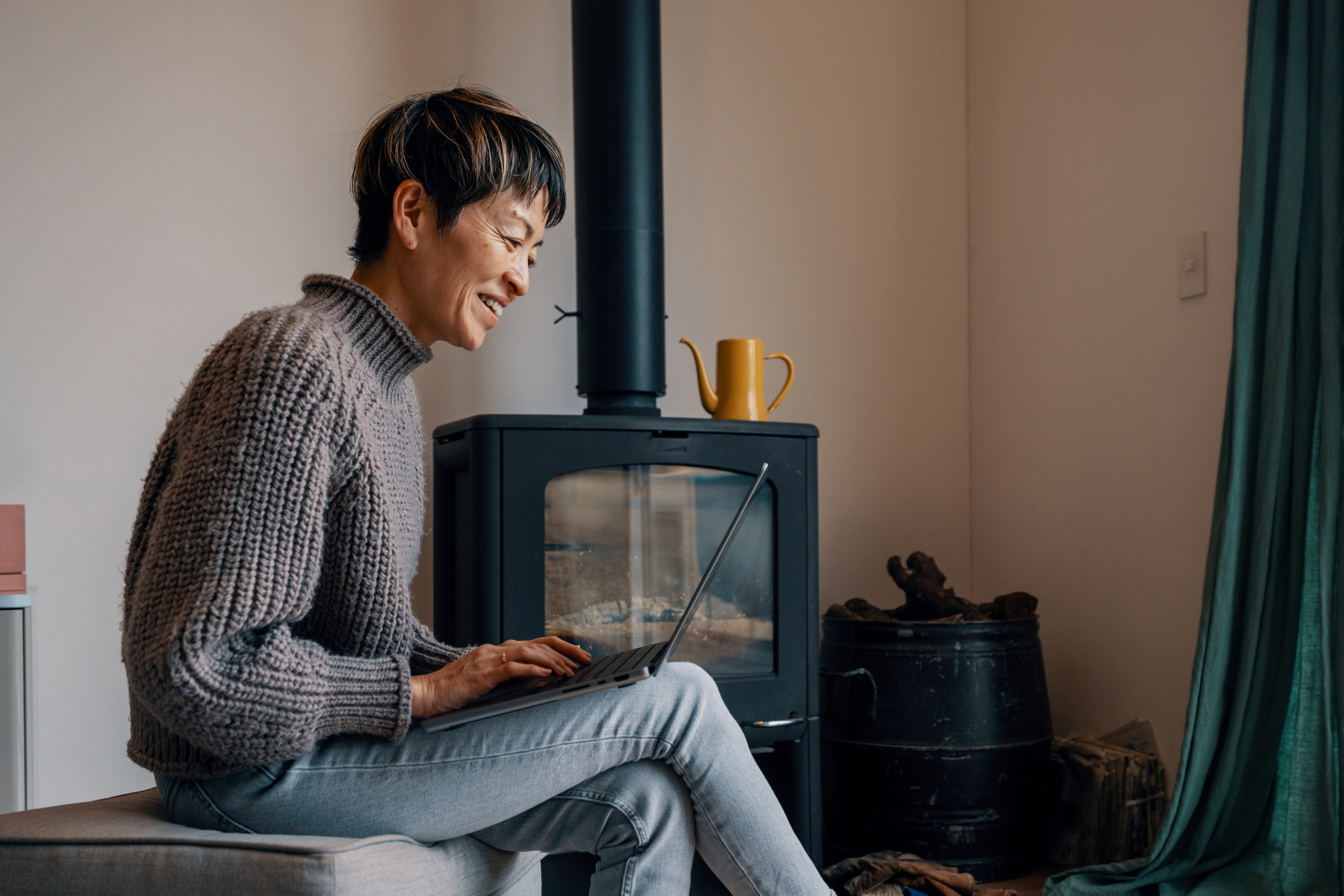 Mature woman using a laptop in front of a wood burning stove in a modern Japanese home