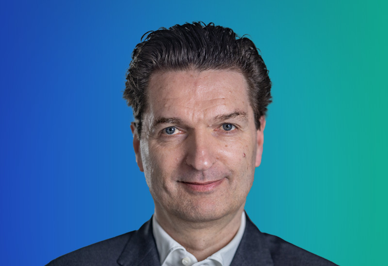 A person in formal attire with a gradient blue and green background.