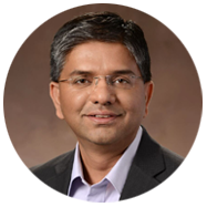 2A person wearing a dark suit jacket and light-colored collared shirt against a brown gradient background.