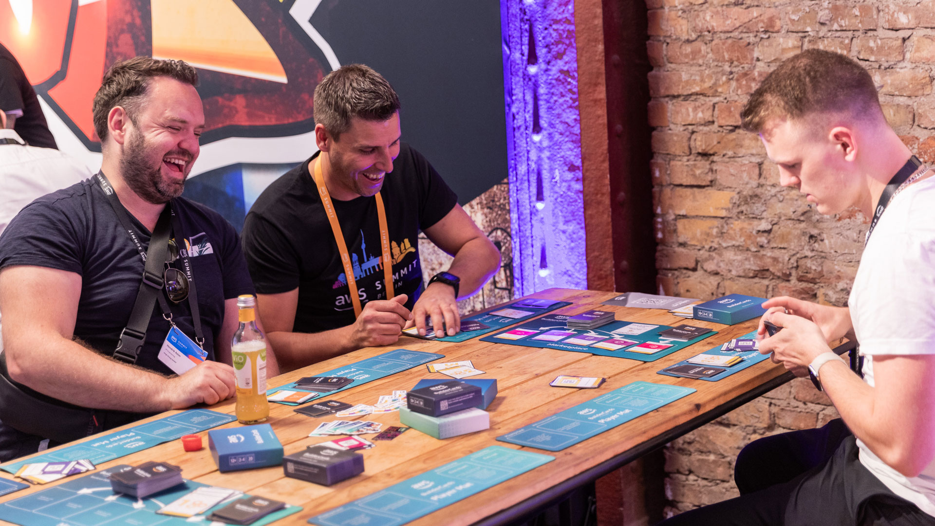 People sitting at a table playing a card-based strategy game, with colorful cards and game materials spread out.