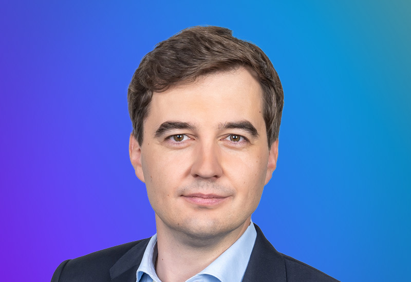 A person in formal attire against a gradient blue and purple background.