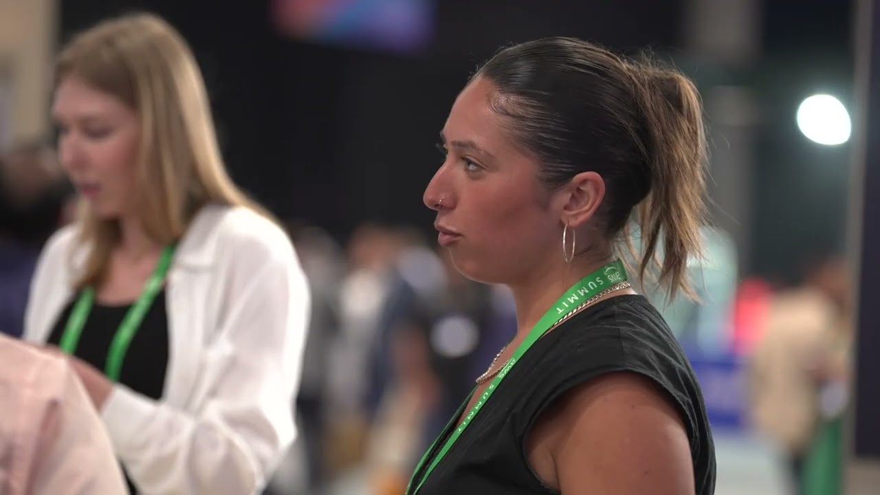 Two individuals wearing green lanyards in a busy indoor event setting.