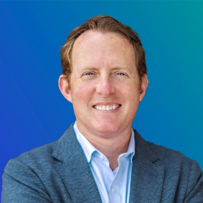 A person wearing a blue blazer and white collared shirt against a gradient blue background.