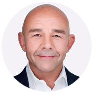 2A person wearing a white collared shirt and dark blazer against a plain background.