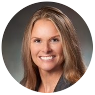 2A person with long, light brown hair wearing a dark blazer, set against a neutral background.