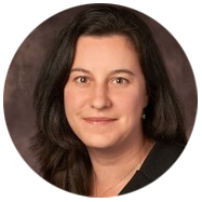 2A person with long dark hair wearing a black top, set against a dark background.