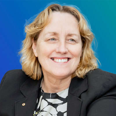 A person with blonde hair wearing a black blazer and patterned blouse against a blue gradient background.
