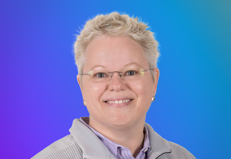 A person with short, light-colored hair wearing a gray sweater and a striped shirt, set against a gradient blue and purple background.