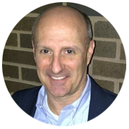 2A person wearing a suit jacket and collared shirt stands in front of a brick wall.