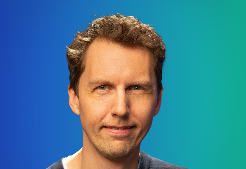 A professional headshot of a man in front of a blue-to-green gradient background