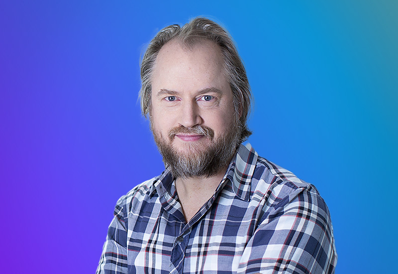 Headshot of a person with light hair and beard wearing a plaid shirt, on a blue to teal gradient background. Used for AWS Summit Stockholm event promotions.