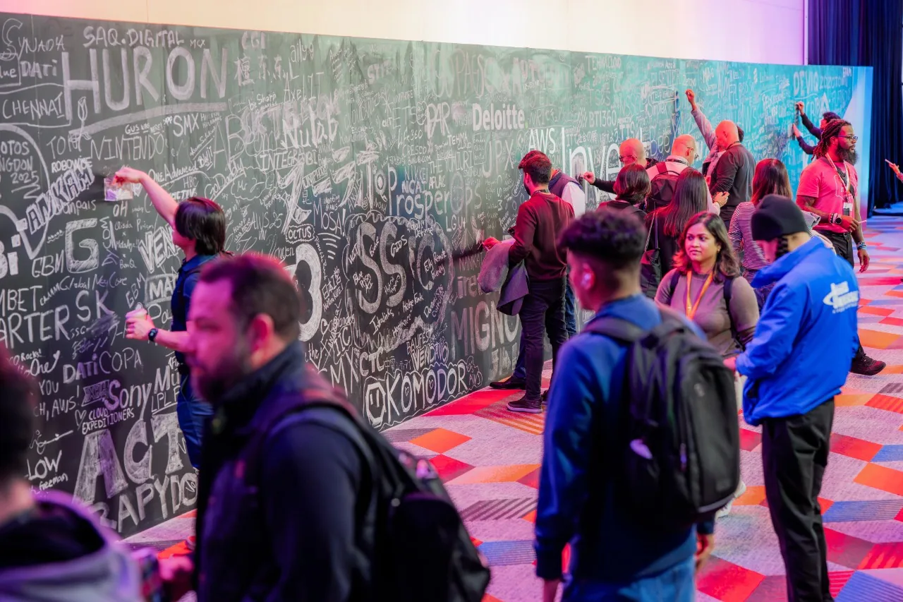 re:Invent attendees adding handwritten messages to a large chalkboard wall.