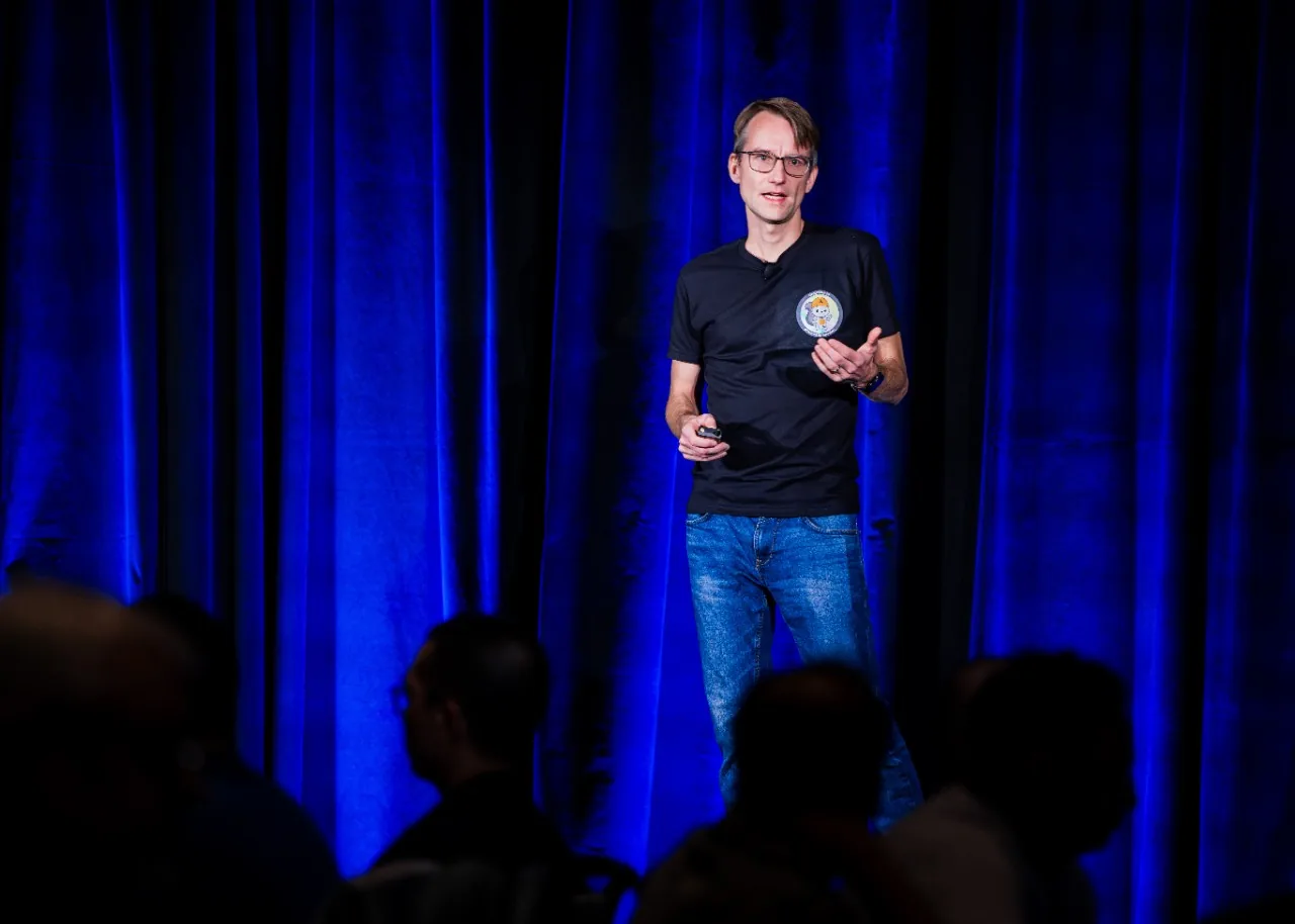 Speaker presenting on stage in front of blue stage curtains.