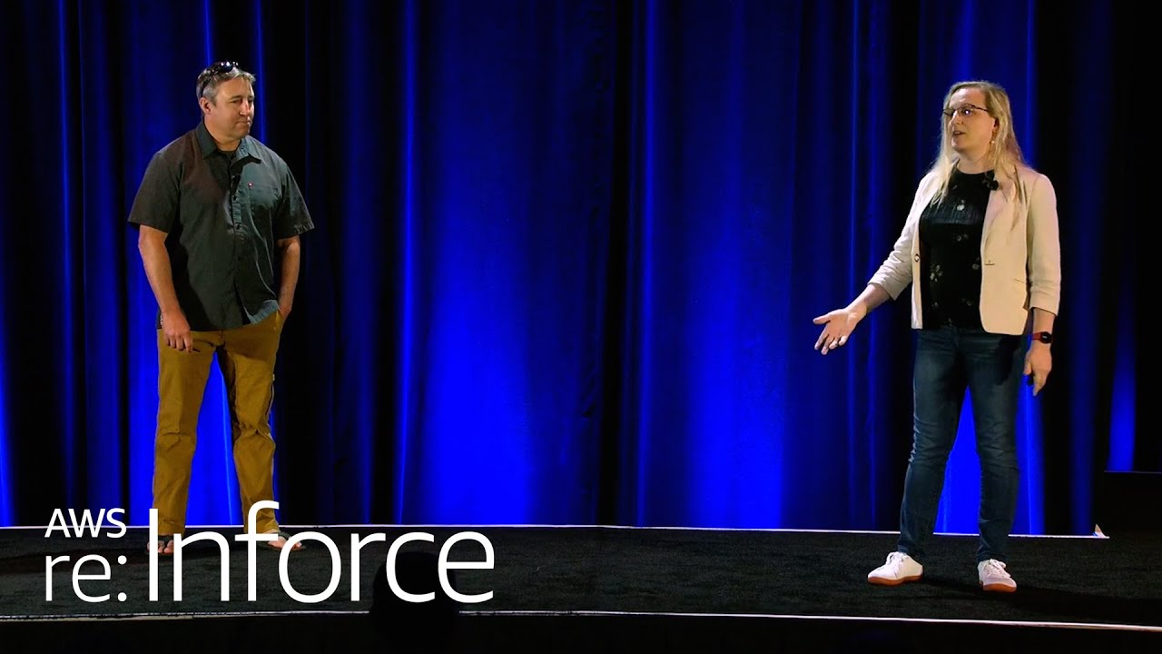 Two presenters stand on a stage with a blue curtain backdrop at an AWS re:Inforce event.
