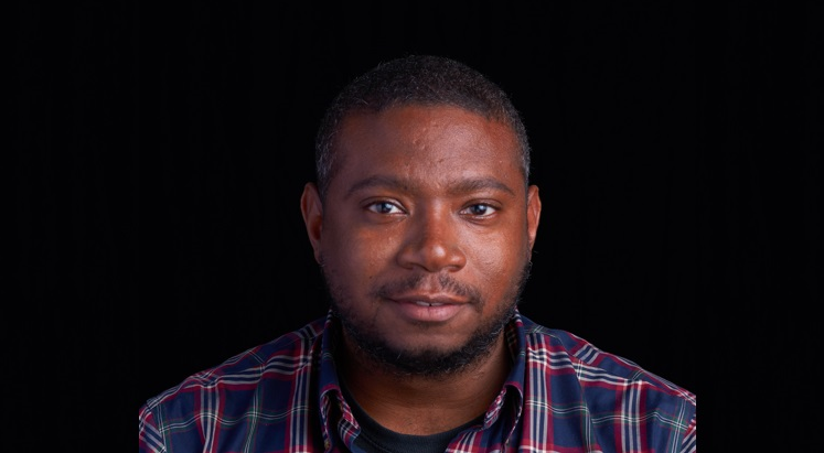 A person wearing a red and blue plaid shirt against a black background.