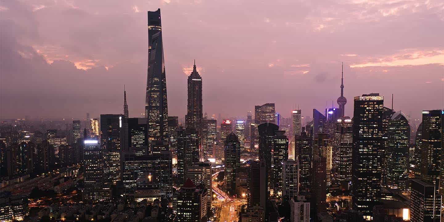 Shanghai city skyline at dusk with illuminated skyscrapers and a purple-pink sky.