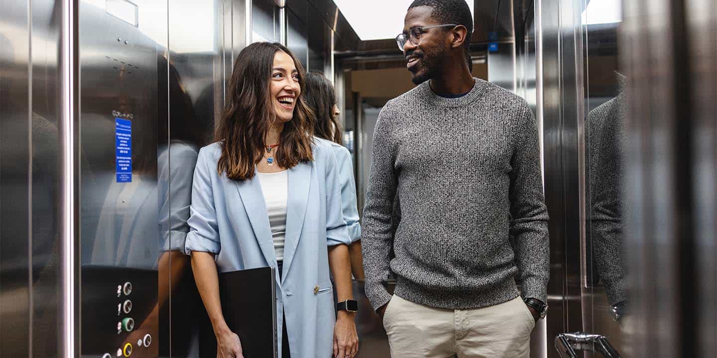 A man and a woman smiling and conversing while riding in a modern office elevator.