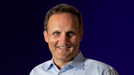 A person wearing a light blue collared shirt against a dark blue background.