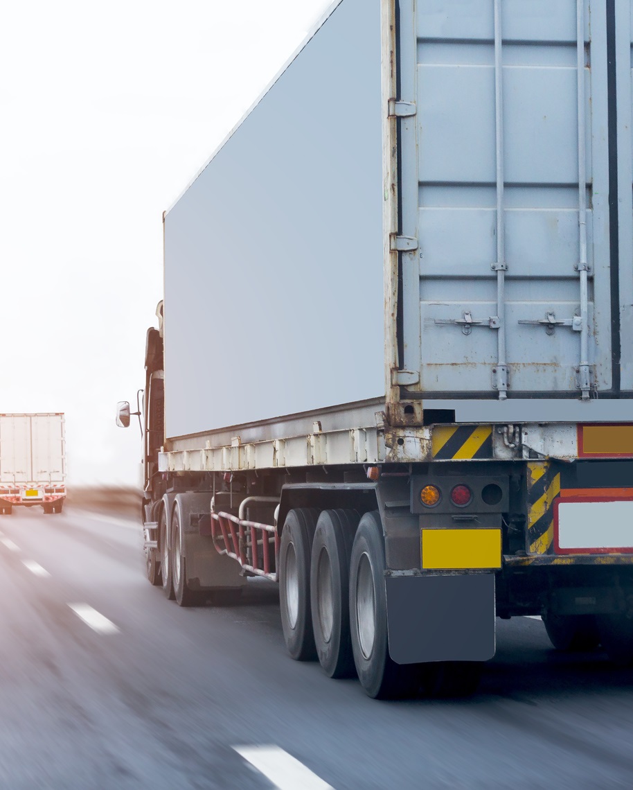 Close-up of a large truck trailer driving on a highway with another truck visible in the distance.